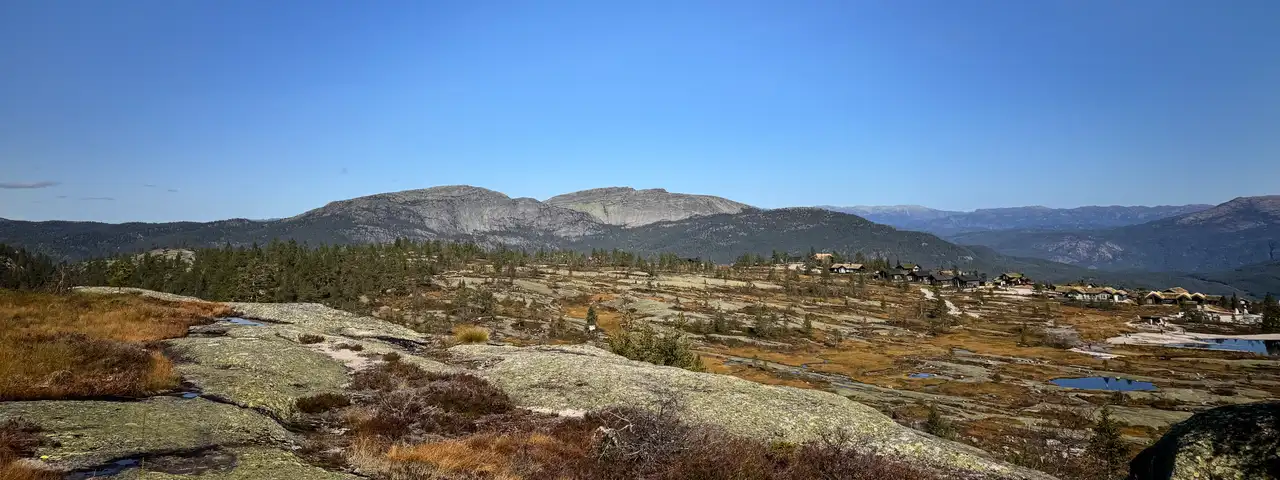 Utsikt fra et svaberg i Vrådal utover hyttefelt, små tjern og avrundede fjelltopper under klar blå himmel.